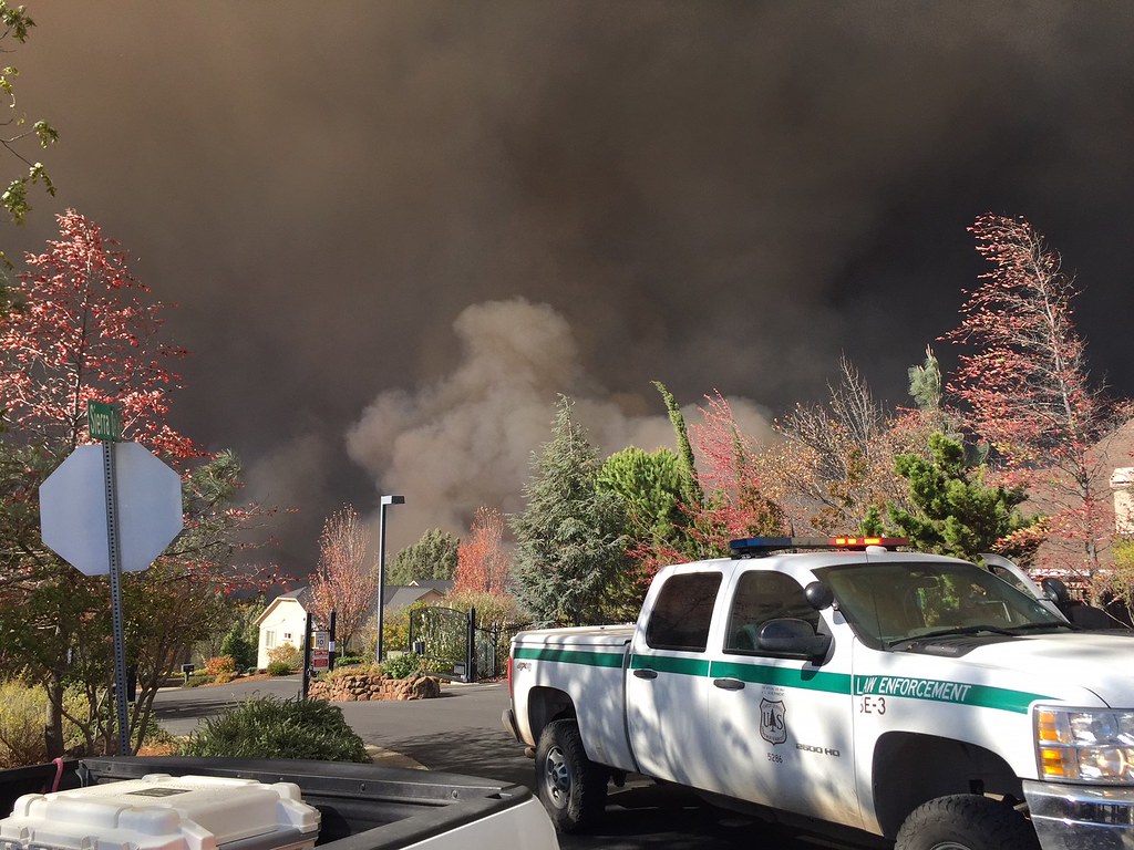 truck parked in front of houses with smoke from a fire in the background