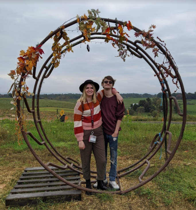Two people stand outside on a cloudy day underneath a leaf-adorned arbor.