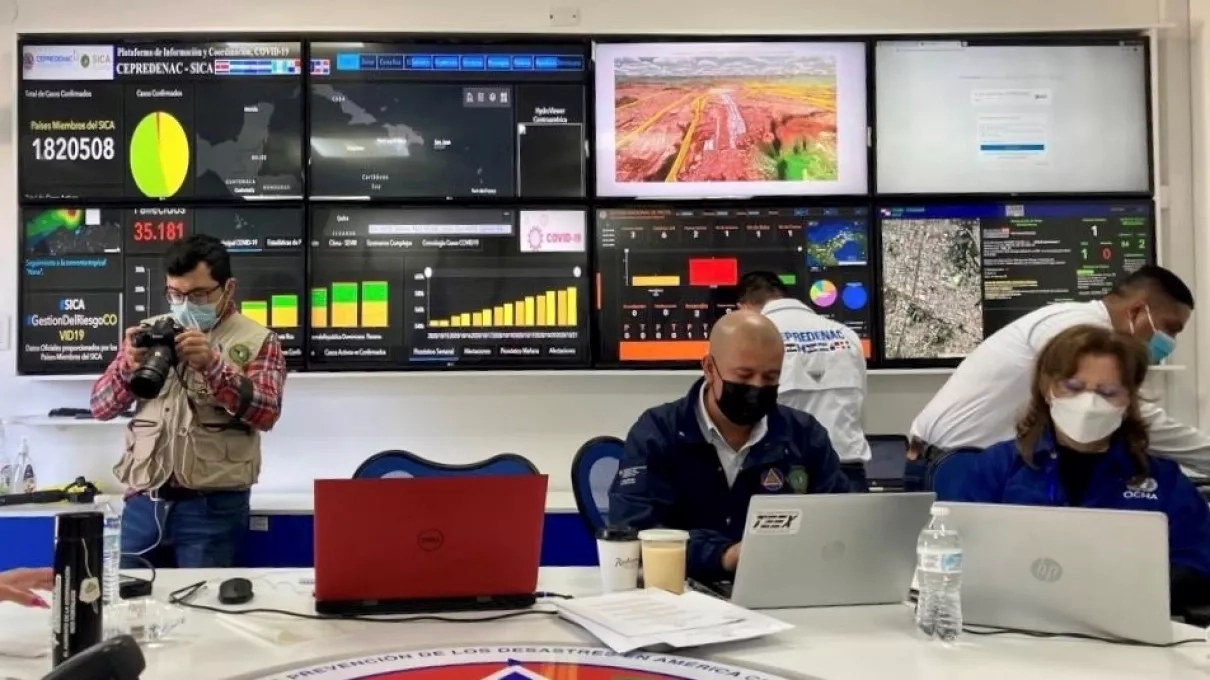 Photo of Scientists and responders look at data in the Emergency Operations Center during the earthquake simulation activity. Navteca immersive visualization is top screen, third from left.