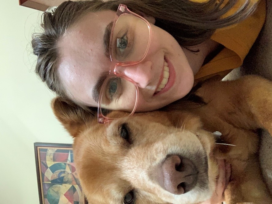 A close up photo of Teresa Purello, smiling and wearing pink glasses, and a brown dog.