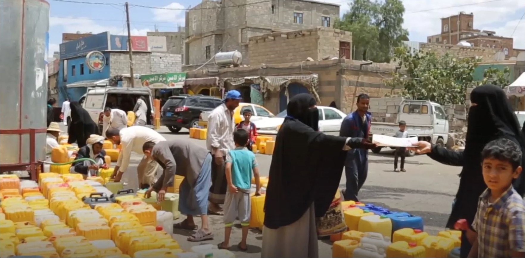 A group of people in Yemen gather around yellow and blue containers with clean water. Image description: A group of people in Yemen gather around yellow and blue containers with clean water.