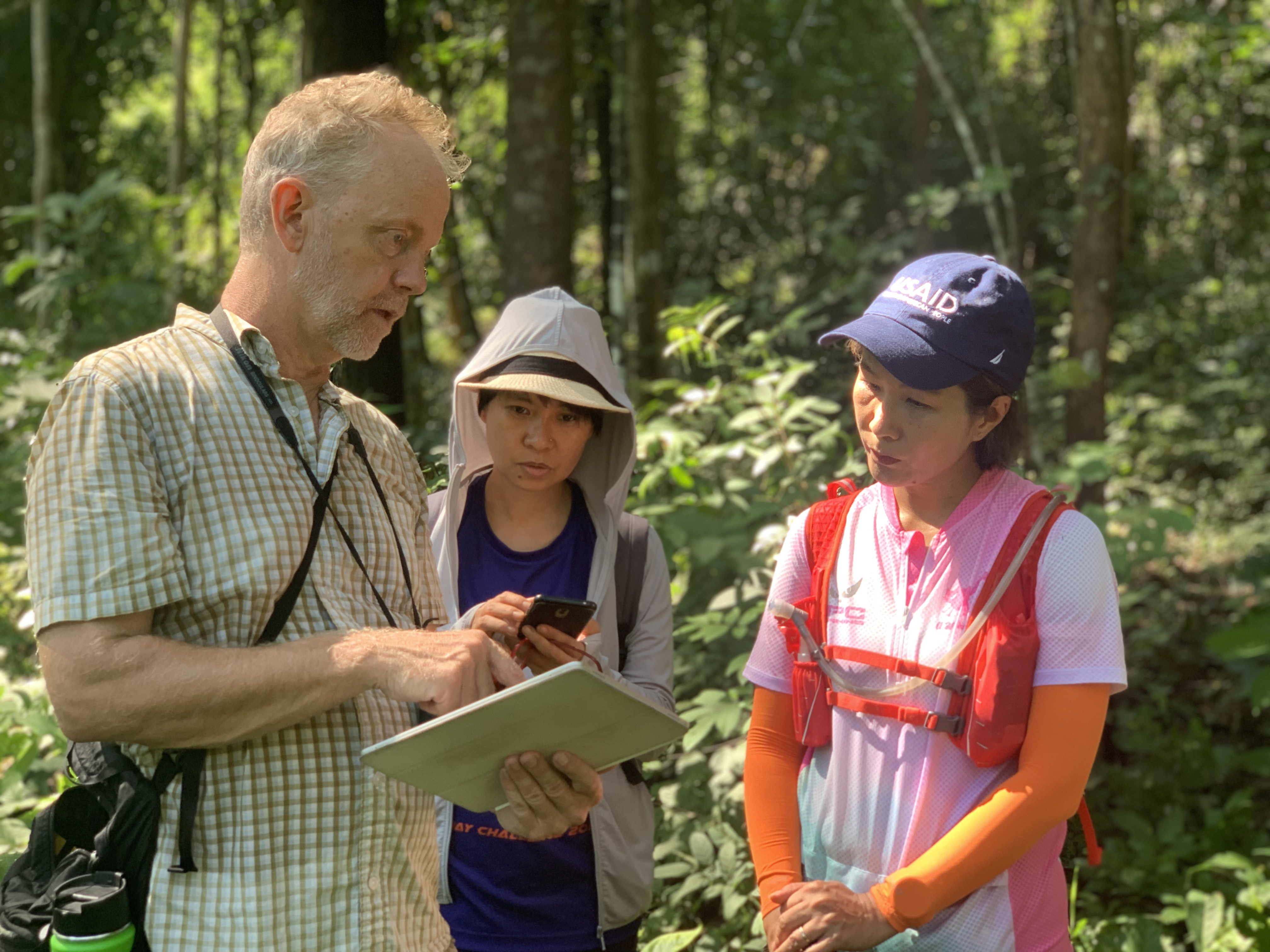 three people standing in a forest reviewing content on a tablet