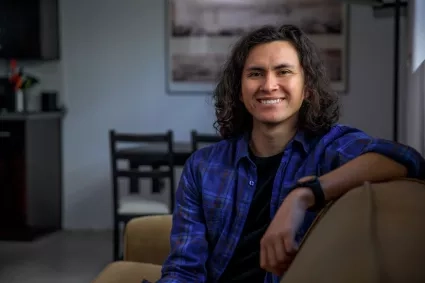 Man with curly hair leans arm on couch and smiles in a living room