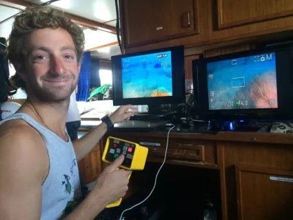 Man with curly hair uses remote control to view underwater images on two screens