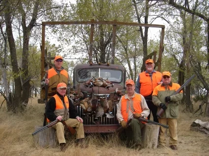 Five men posing in hunting vests with guns in front of a truck