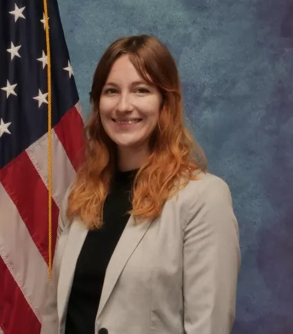 Woman in blazer poses for official portait in front of Amerian Flag