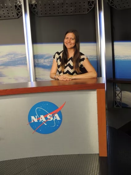 Woman with long hair sits behind a desk with NASA logo on it 