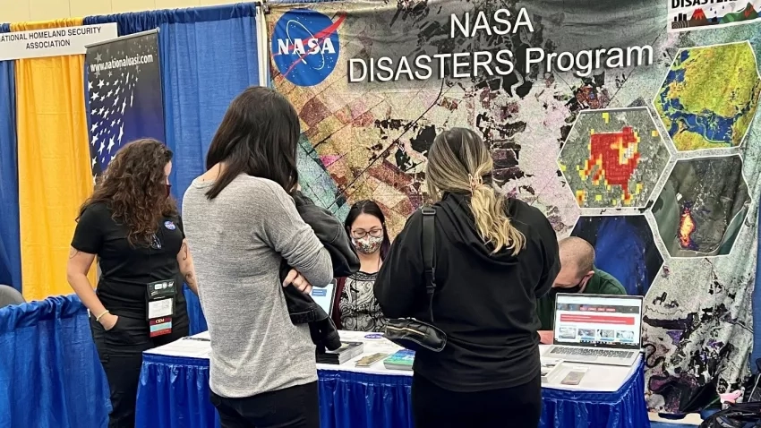 Jennifer Paris (left) looks on as Margaret “Maggie” Glasscoe (third from left) explains NASA Disasters current research portfolio to visitors at the International Association of Emergency Managers (IAEM) Conference in Grand Rapids, Michigan, Tuesday, Oct. 19, 2021 Credits: NASA/Seph Allen