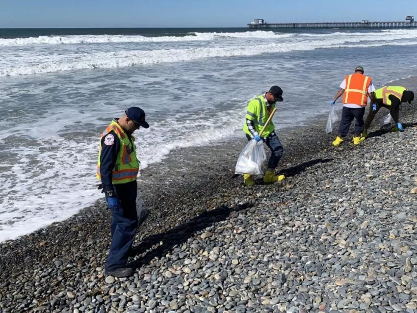 Contractors on a hotshot team remove tar balls from shores in Oceanside Harbor Beach in San Diego County, in response to the Orange County oil spill, Oct. 12, 2021. Credits: U.S. Coast Guard/Petty Officer 3rd Class Alex Gray)