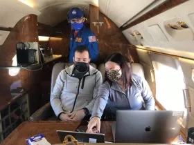 three people looking at a laptop while on a plane