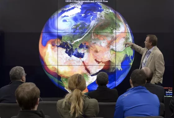 photo of man pointing at an image of the Earth while speaking to an audience