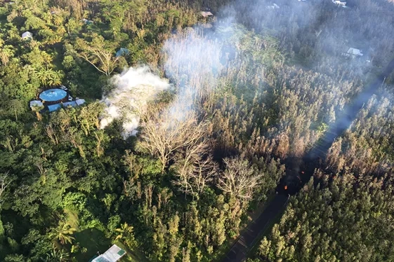 picture taken from above showing a few structures nestled among a forest with smoke rising from treetops