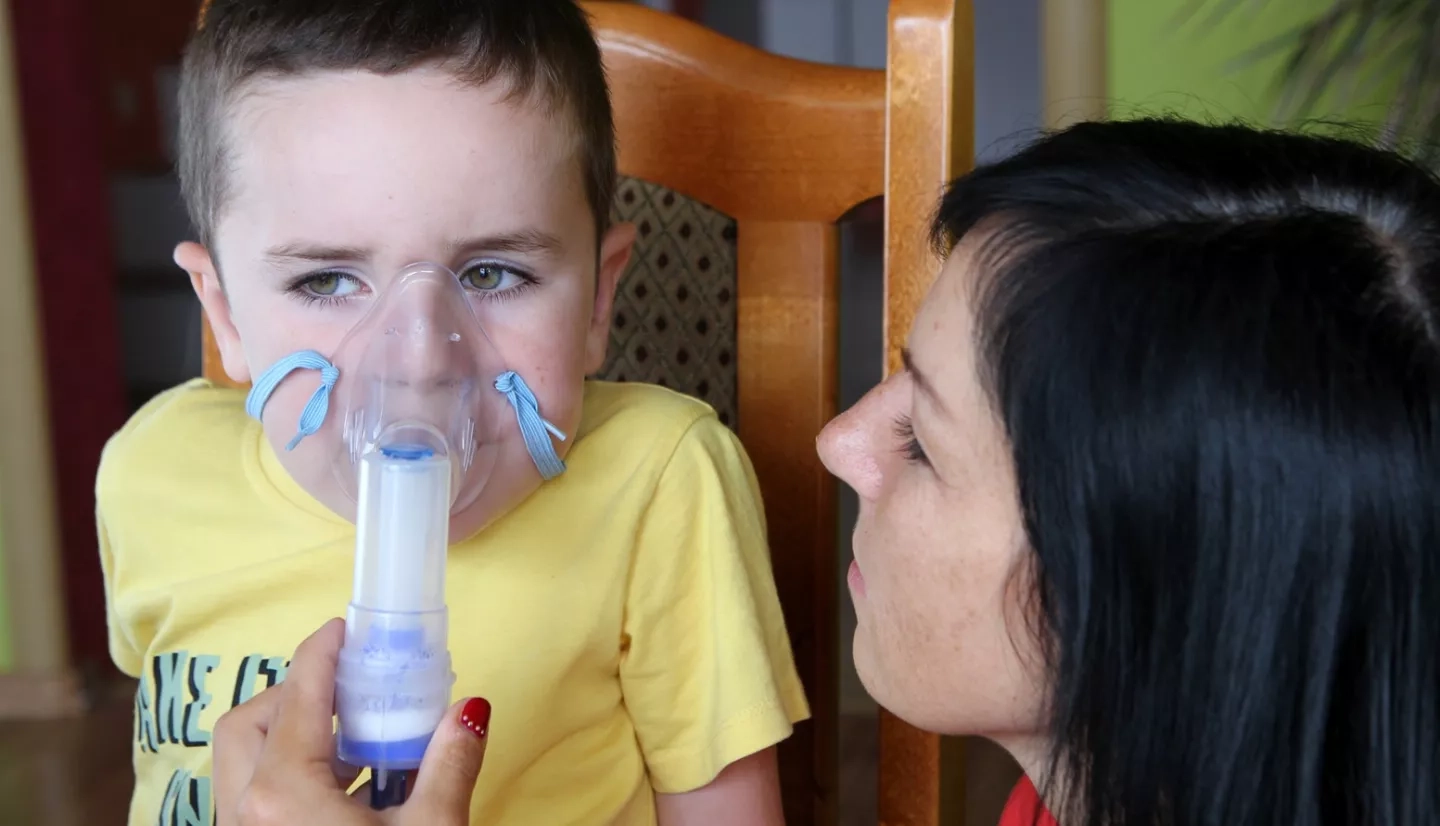 woman helps child use an inhaler