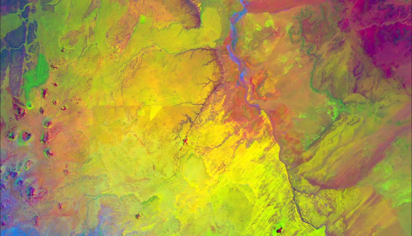 Color composite image portraying Wupatki Basin in northwestern Arizona, derived from 2021 LANDSAT 8 OLI/TIRS imagery. This image depicts Pinyon-Juniper Woodlands (PJW), among other vegetation, between the river and mountains in a light green color. Thermal Infrared (TIR) occupies the red band, while the green and blue bands represent the Modified Normalized Difference Water Index (MNDWI) and the Modified Soil-Adjusted Vegetation Index (MSAVI), respectively. The reduced correlation between bands in this comp