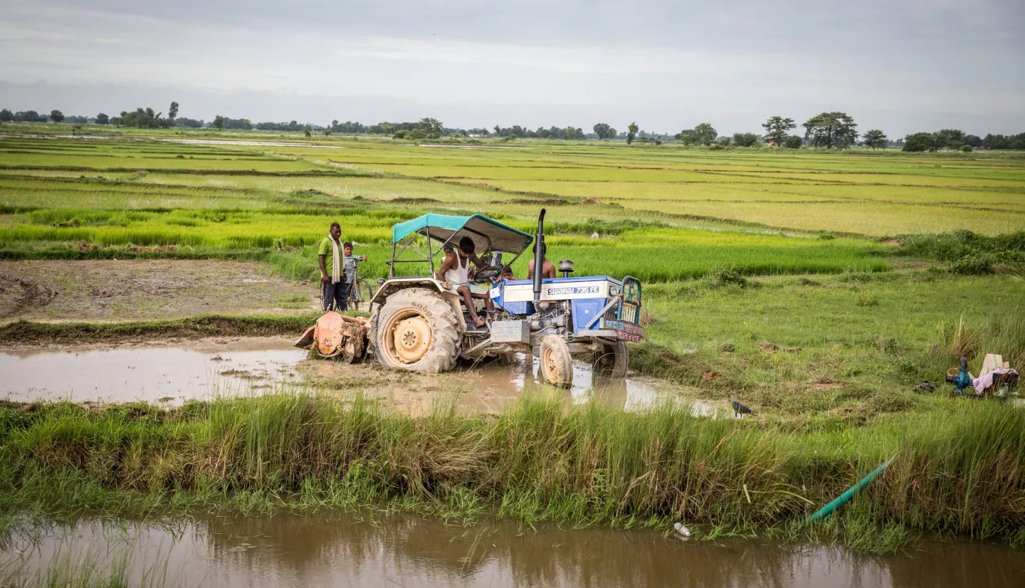 Farmers guide a tractor out of the mud of a large, flat expanse of rice fields in Nepal. Credit: ICIMOD, Jitendra Raj Bajracharya