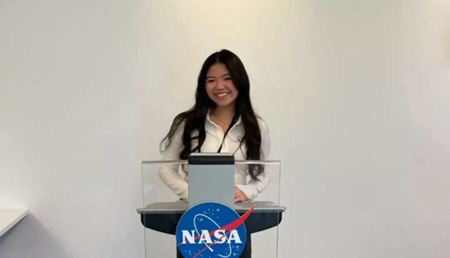 Tiffany at a podium in front of the NASA meatball at the DEVELOP term closeout presentation.
