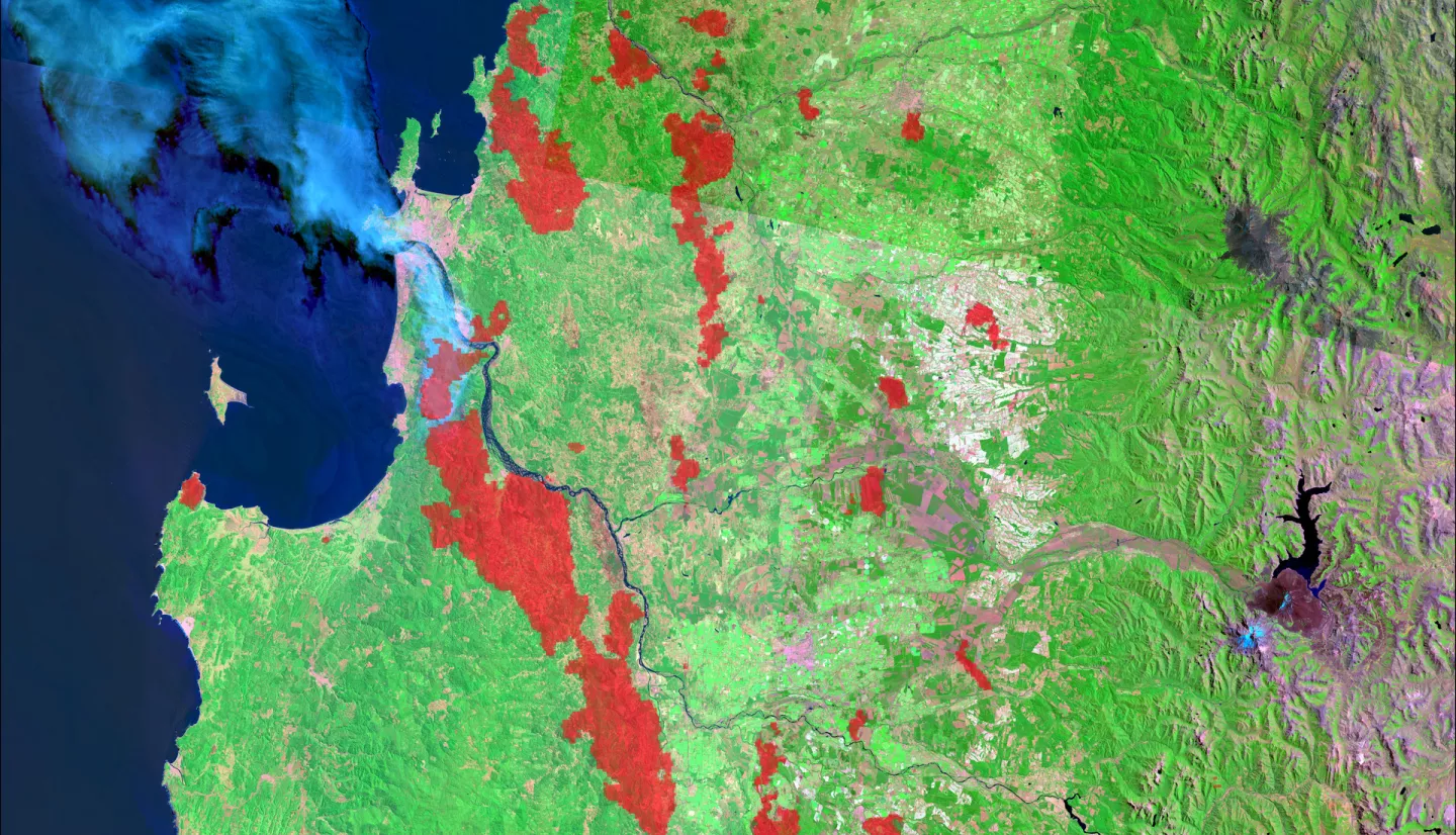 The data come from Landsat 9 OLI and MODIS satellites. The data shows surface reflectance imagery and combined (Terra and Aqua) MODIS burned areas from wildland fires in February 2023. The image shows parts of South-Central Chile covering Región del Maule, Región del Bío-Bío, and Región de La Araucanía. The processed data show burned areas in the region of interest from wildland fires and the smog from the fires. Red patches indicate burned areas.