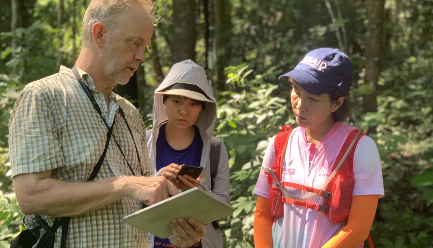 three people standing in a forest reviewing content on a tablet