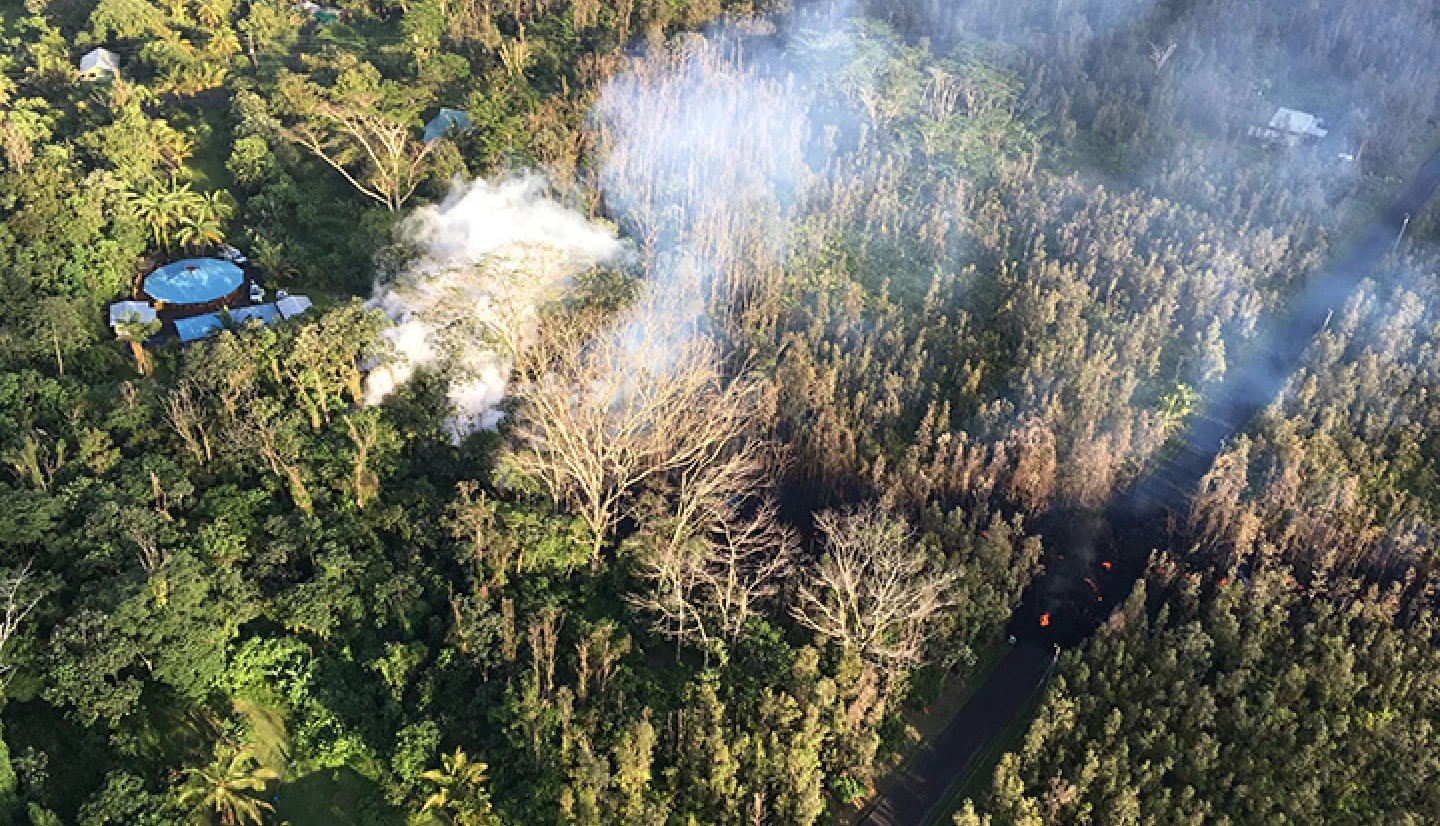 picture taken from above showing a few structures nestled among a forest with smoke rising from treetops