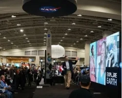 Photo of man on stage gesturing toward a wall of video screens