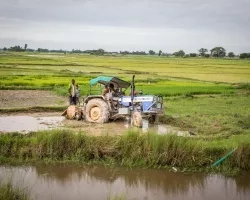 Farmers guide a tractor out of the mud of a large, flat expanse of rice fields in Nepal. Credit: ICIMOD, Jitendra Raj Bajracharya