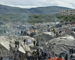 Photograph of rubble and destroyed buildings in the aftermath of the 2023 Turkiye earthquakes, with rescue workers and examining the wreckage. 