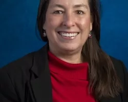 Amber Soja, smiling in front of a blue backdrop, in a red top with a black blazer