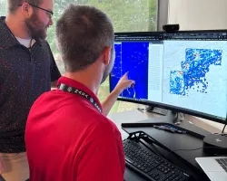 Two scientists examine a computer screen with hurricane data. 
