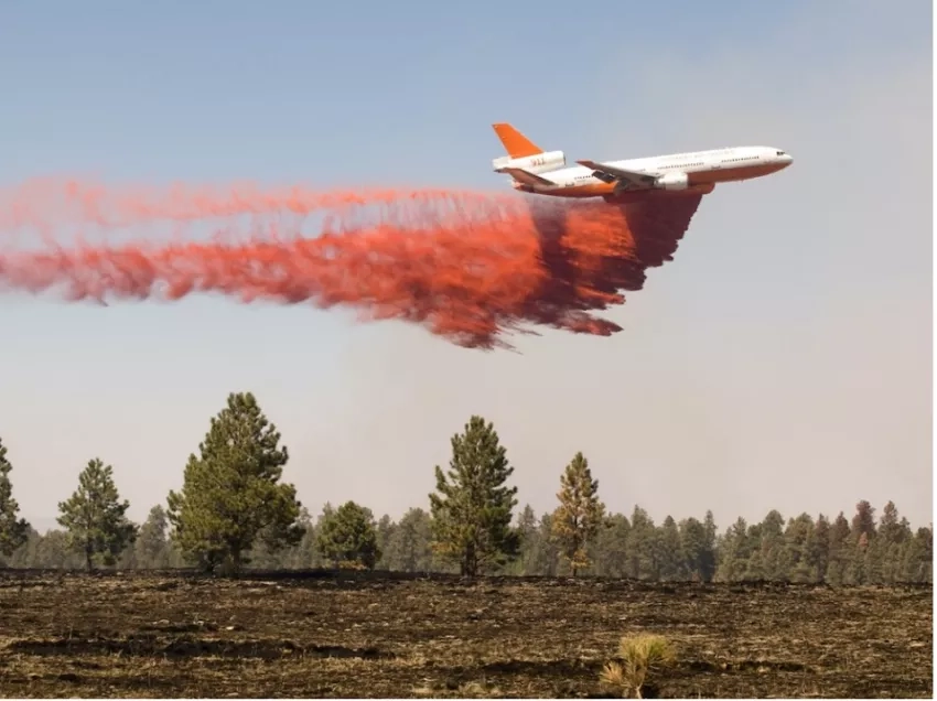 photo of plane dropping red fire retardant material over an open field