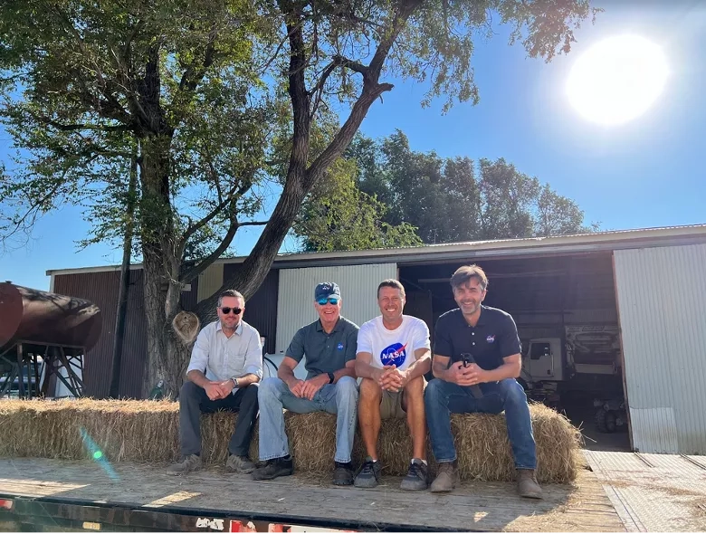 NASA's Chris Hain, Brad Doorn, and Forrest Melton take a seat on hay bales with Derek Klingenberg (White NASA shirt), producer of YouTube channel, Farmer Derek. Credits: NASA