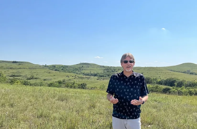 man standing in Kansas prairie with herd bison in the far background