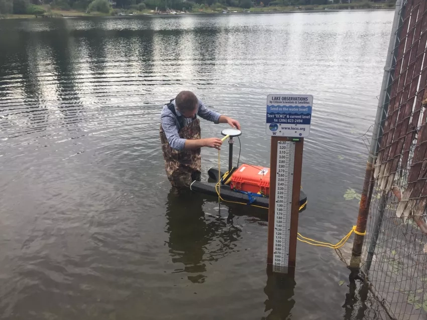 photo of a man in a lake next to a gauge and a small floating device