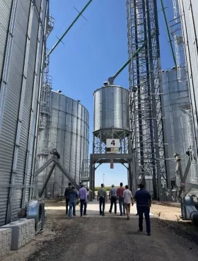 a photo of a group of people walking through massive silver metal silos that hold corn